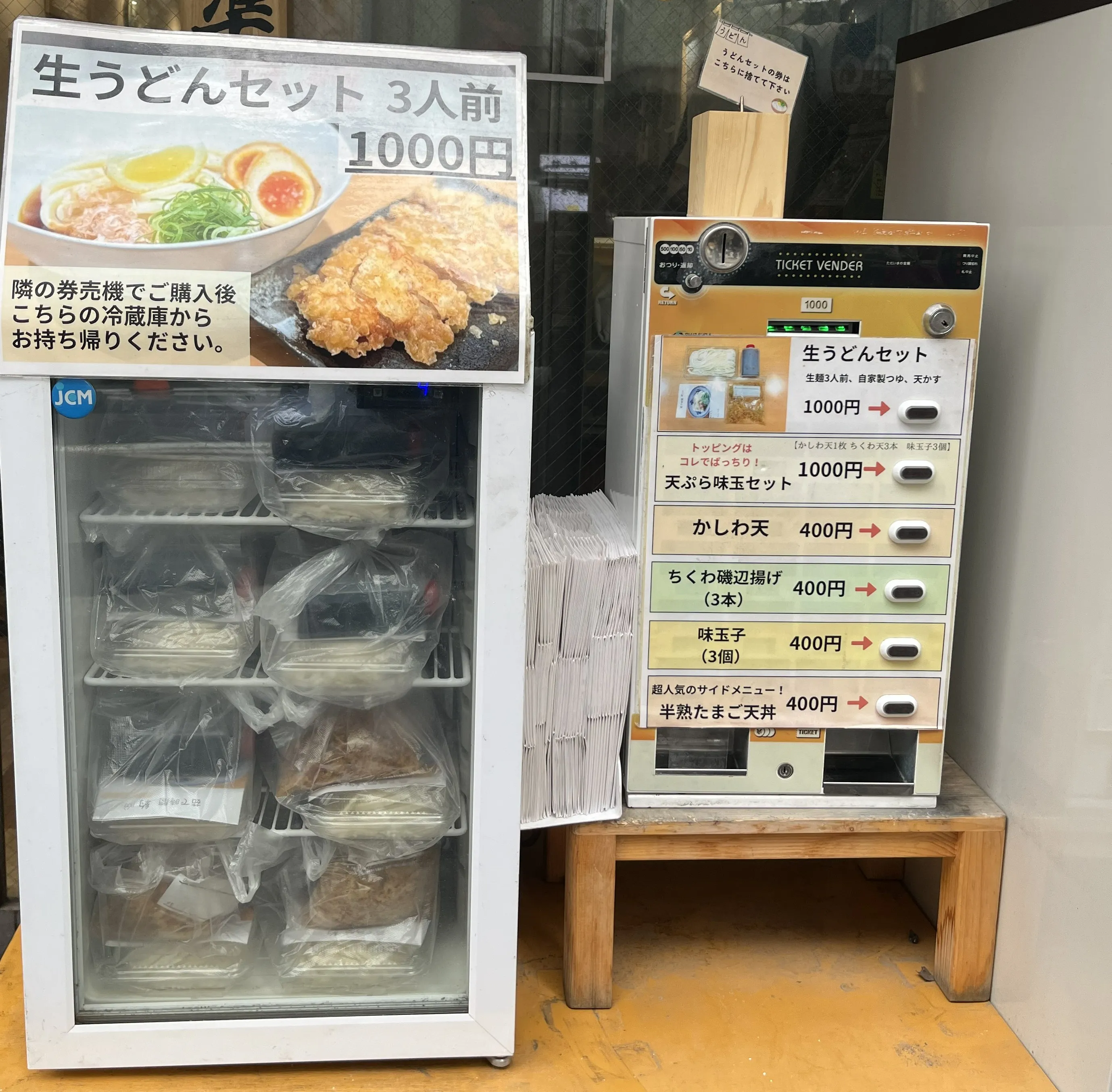 店頭の券売機と冷蔵庫に並ぶうどん宗のテイクアウトメニュー（生うどんセット 3人前 1,000円）