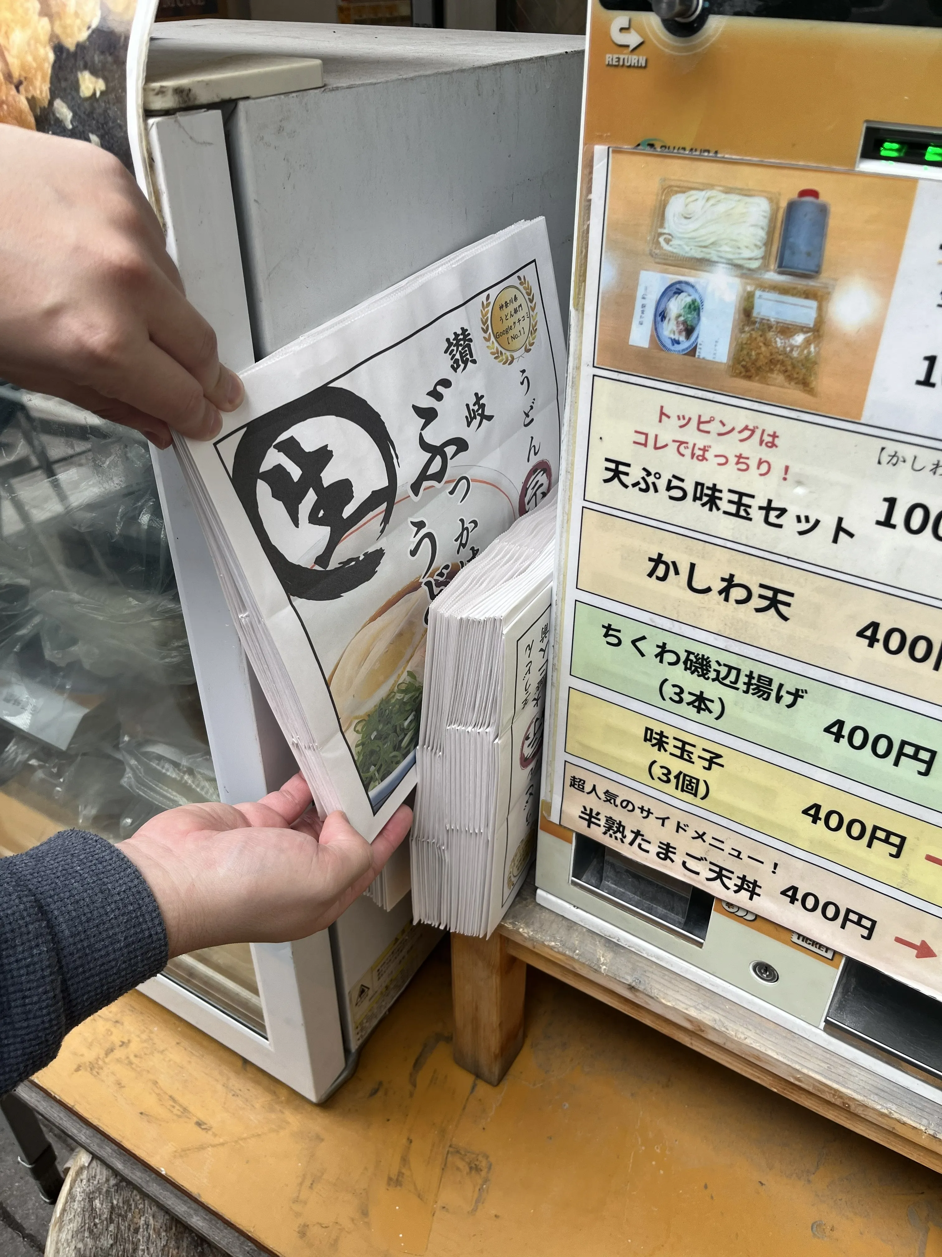 店頭の券売機と冷蔵庫から取り出すうどん宗のテイクアウト紙袋